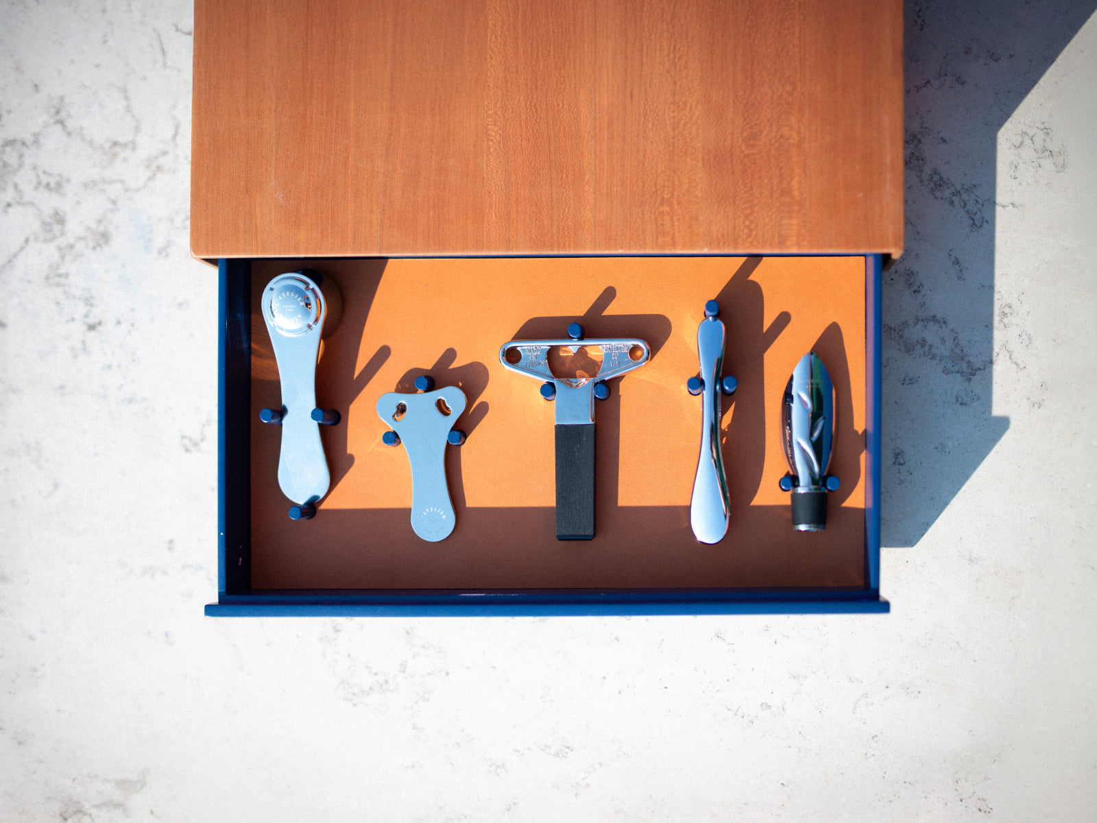 Top view of an open blue exterior drawer with an orange interior, holding neatly arranged wine tools on an orange tray.