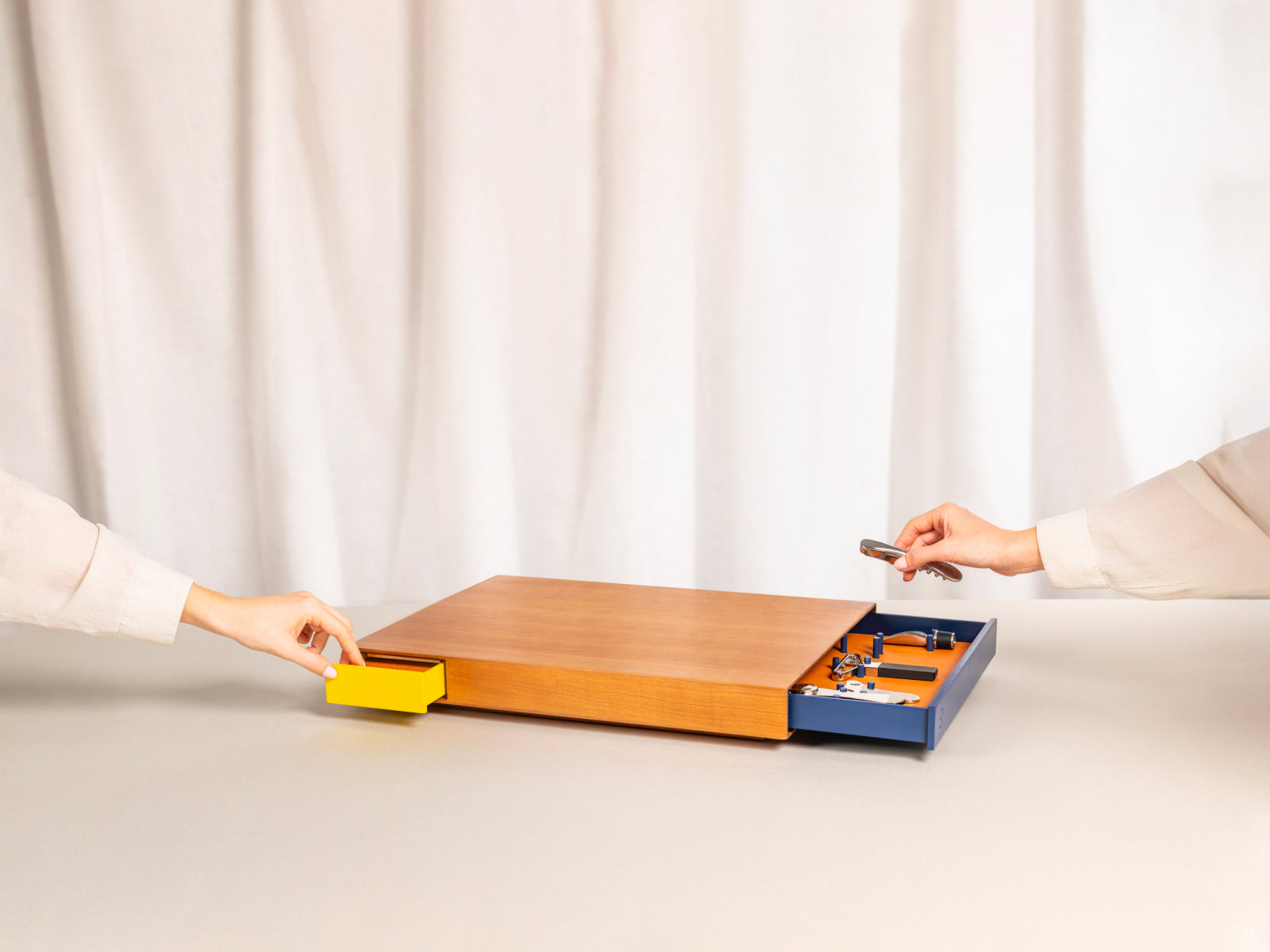 Le Plateau wooden box with yellow pull-out drawer and blue tool tray; hands on each side handle the wine tools.
