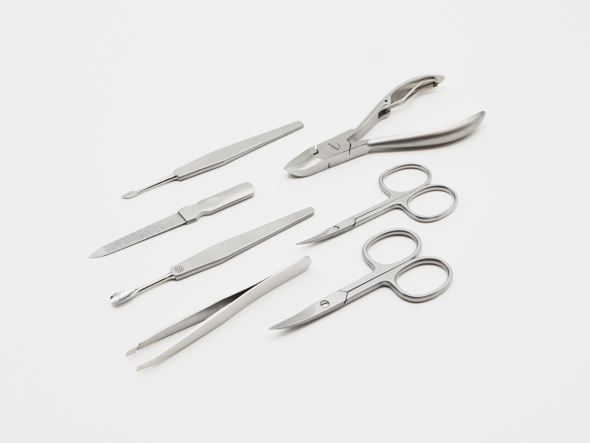 Tempered stainless steel Firenze manicure tools arranged on white background including cuticle and nail scissors and file.