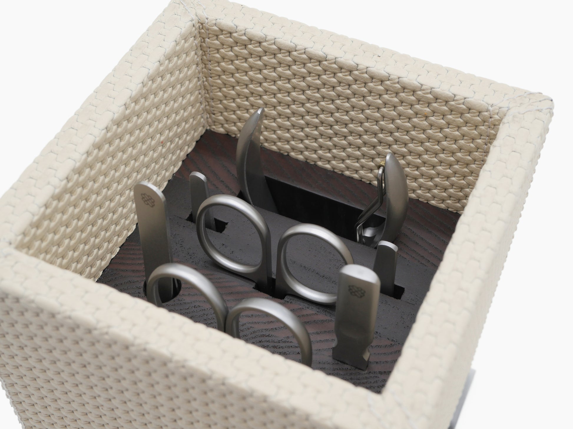 Interior view of Firenze Manicure Set with stainless steel tools arranged in the beige woven box and lid beside it.