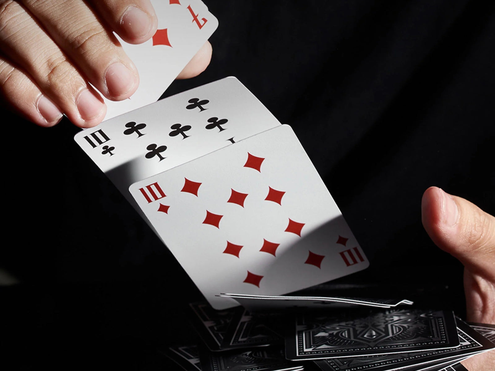 Close-up of a hand displaying Animal Kingdom playing cards with red diamond symbols against a dark background