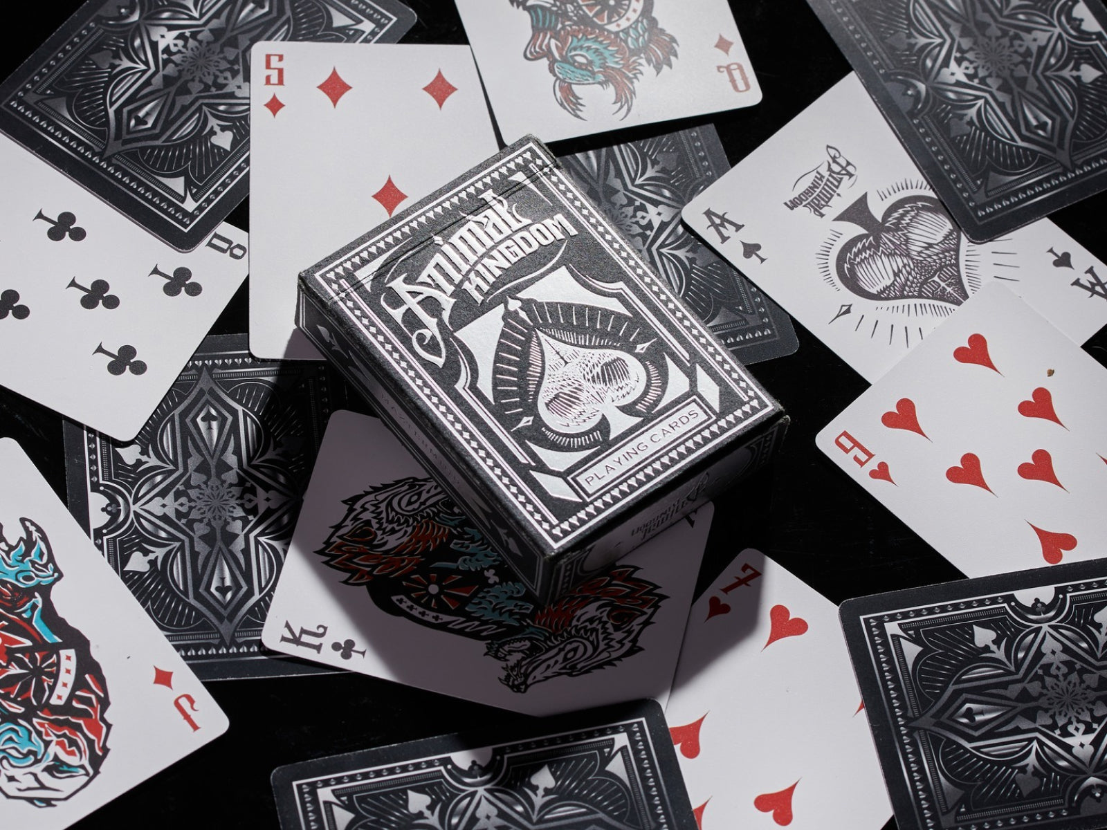 Overhead view of Animal Kingdom playing cards scattered around a decorative black card box.