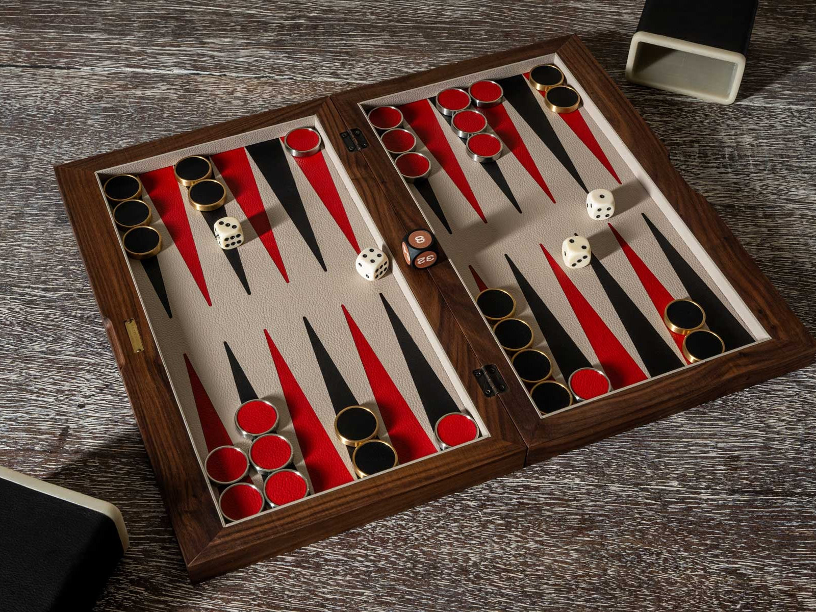 Open walnut backgammon set with red and black points, dice and pieces arranged for play.
