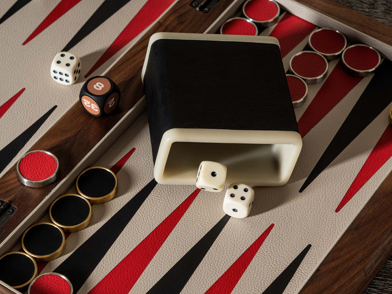 Close up of a premium backgammon board in a walnut frame with red black and tan triangles and dice scattered