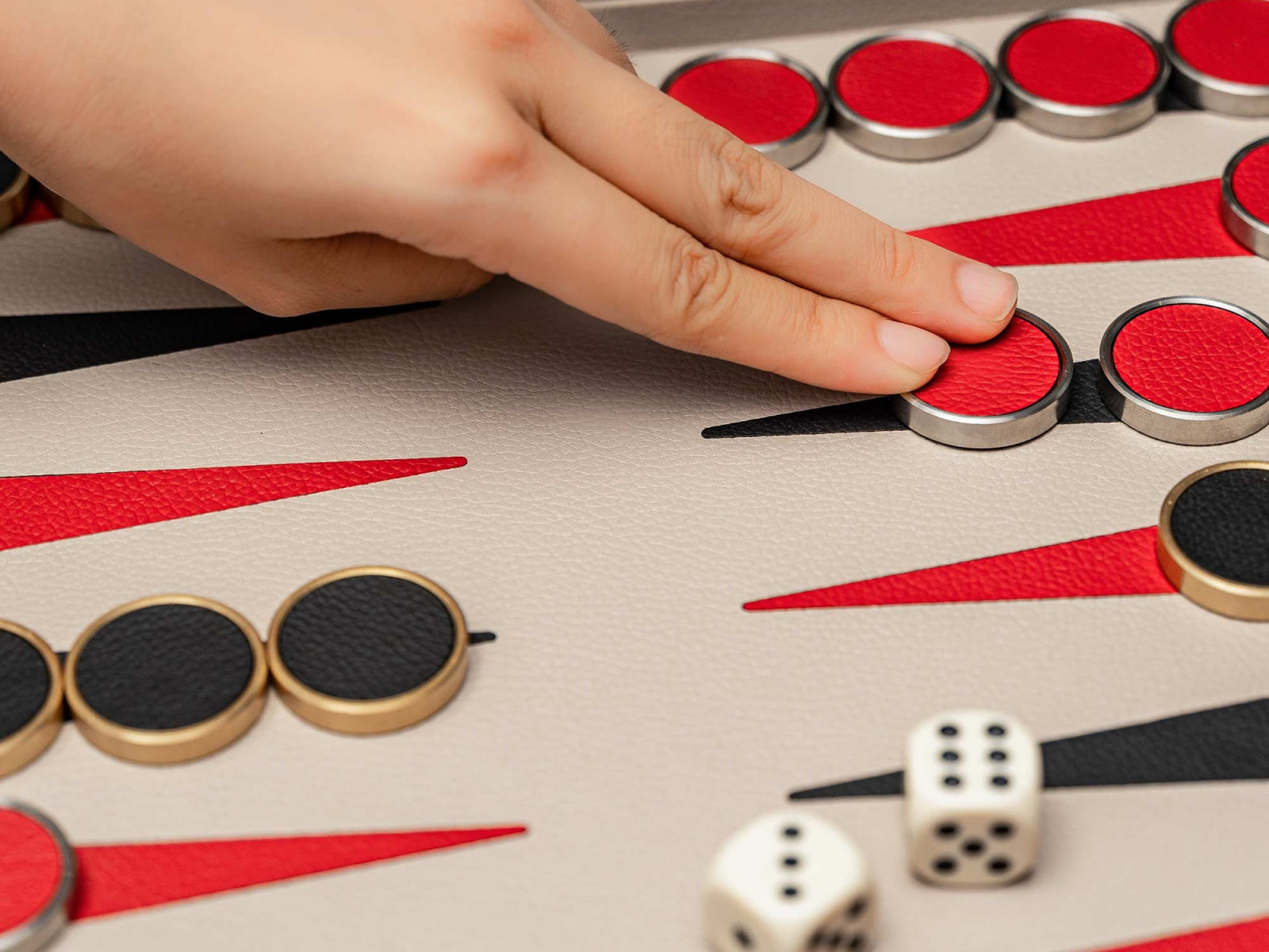 Close up of a hand placing a red backgammon token on a premium walnut backgammon board with leather trim