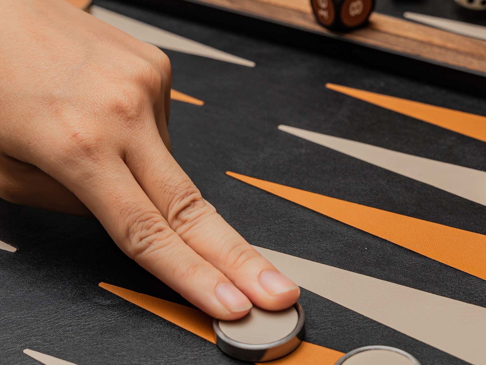 Hand presses a round game piece on a backgammon style surface with orange and beige stripes