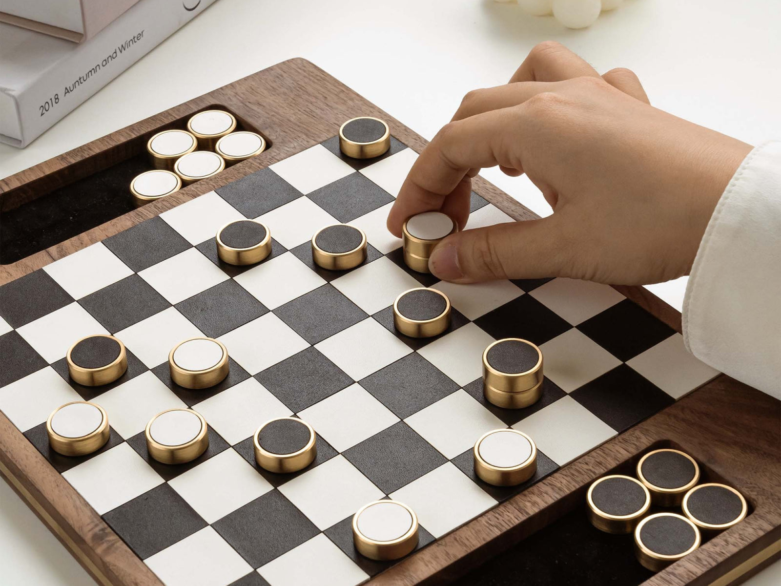 Deluxe Magnetic Wooden Checker on a walnut board with brass edged discs; a hand places a piece