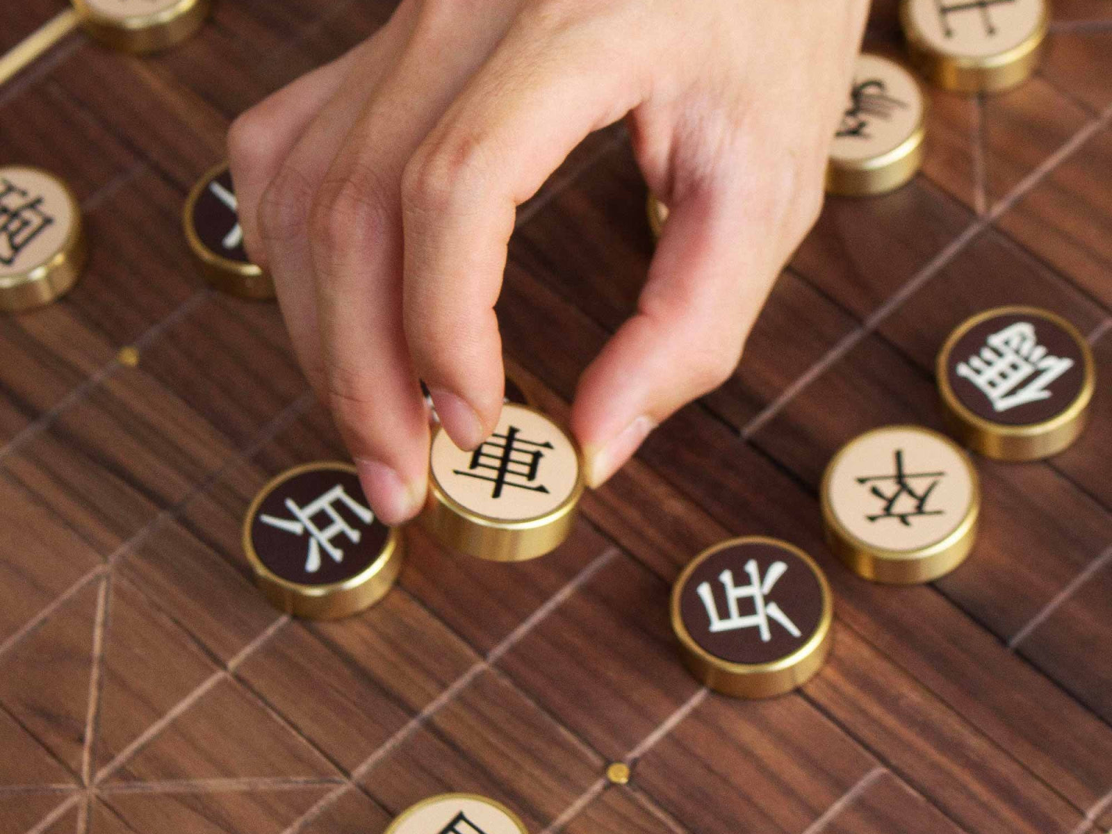 Close up of hands moving bronze Chinese chess pieces on a walnut board with character inscriptions.