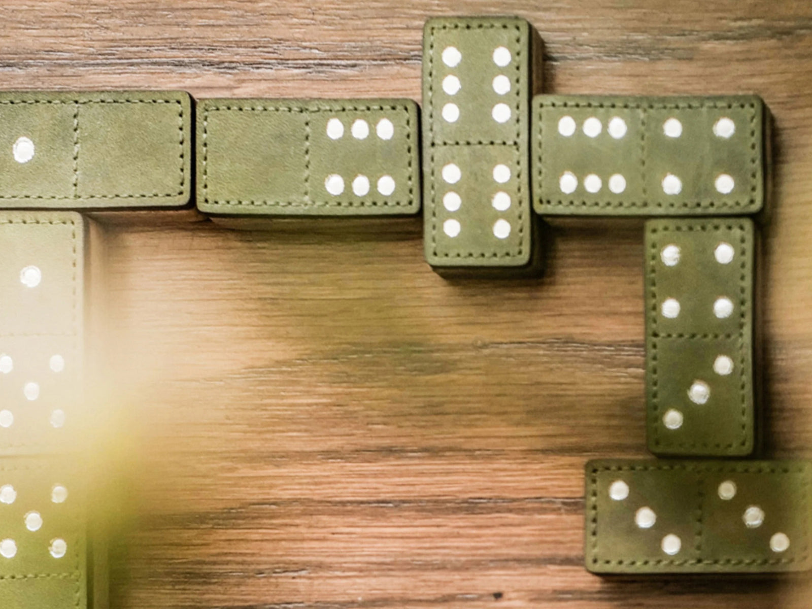 Green leather domino tiles with white pips arranged on a warm wood surface