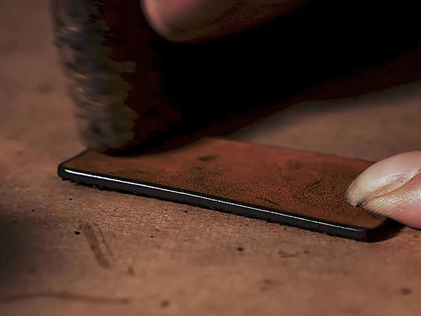 Close-up of olive leather domino tile being pressed on a brown work surface by a fingertip.