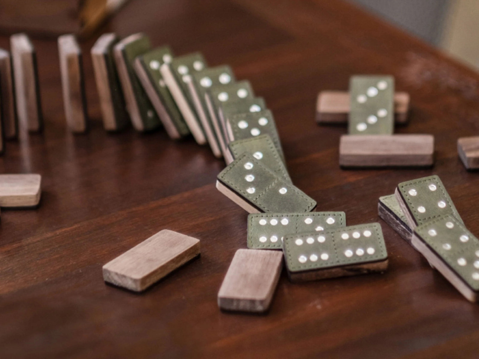 Close-up of green leather domino tiles with white pips on a dark wooden table