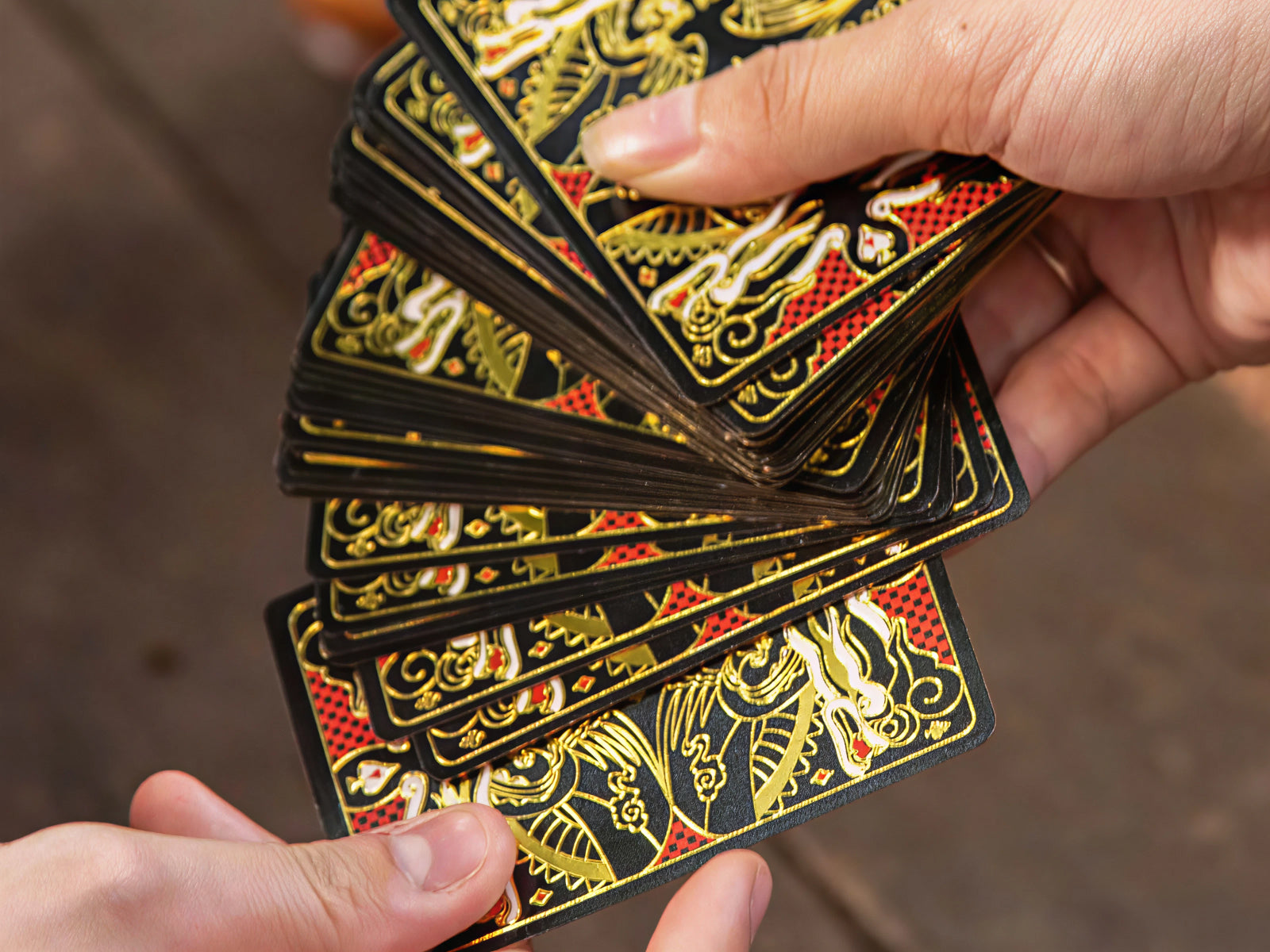 Hands holding a fanned stack of Immortals Playing Cards with ornate gold on black backs.