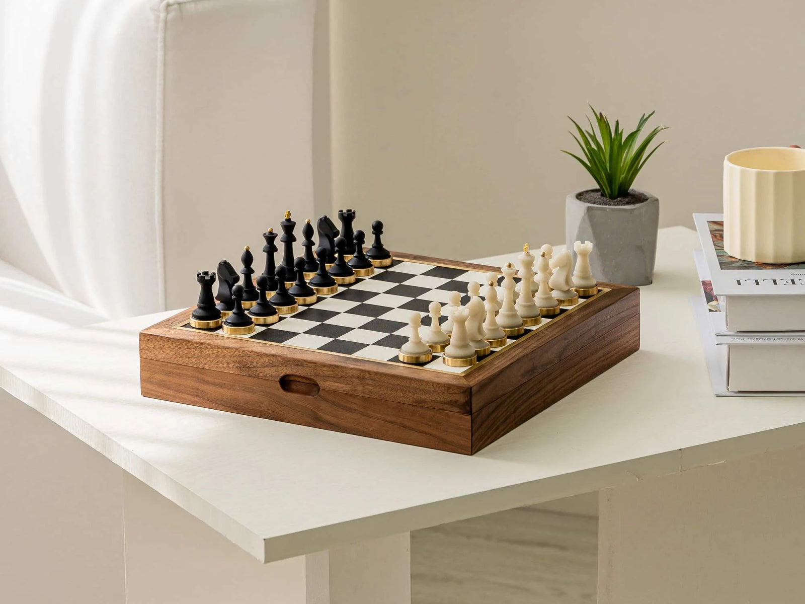 Elegant walnut chess set displayed on a white desk with a small plant and magazines in the background