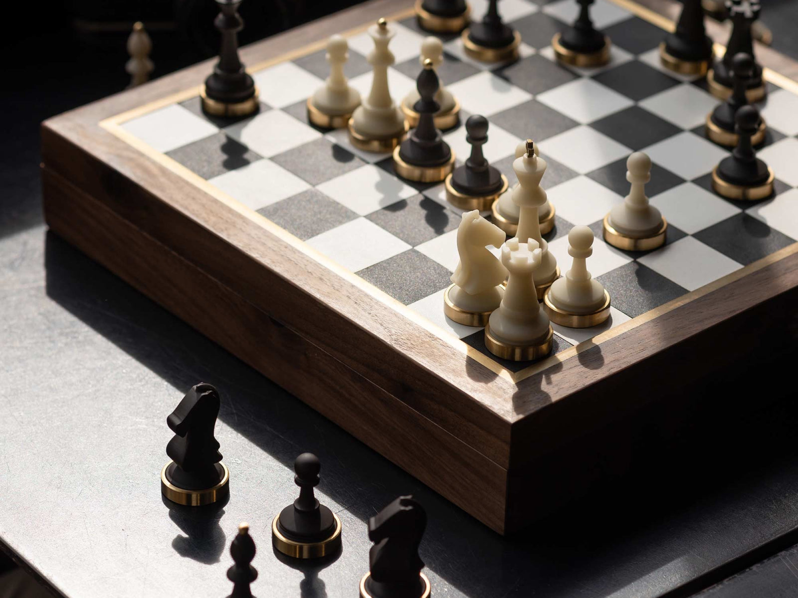 Corner view of a walnut wood chessboard with brass-edged frame and ivory and dark pieces set for a game.