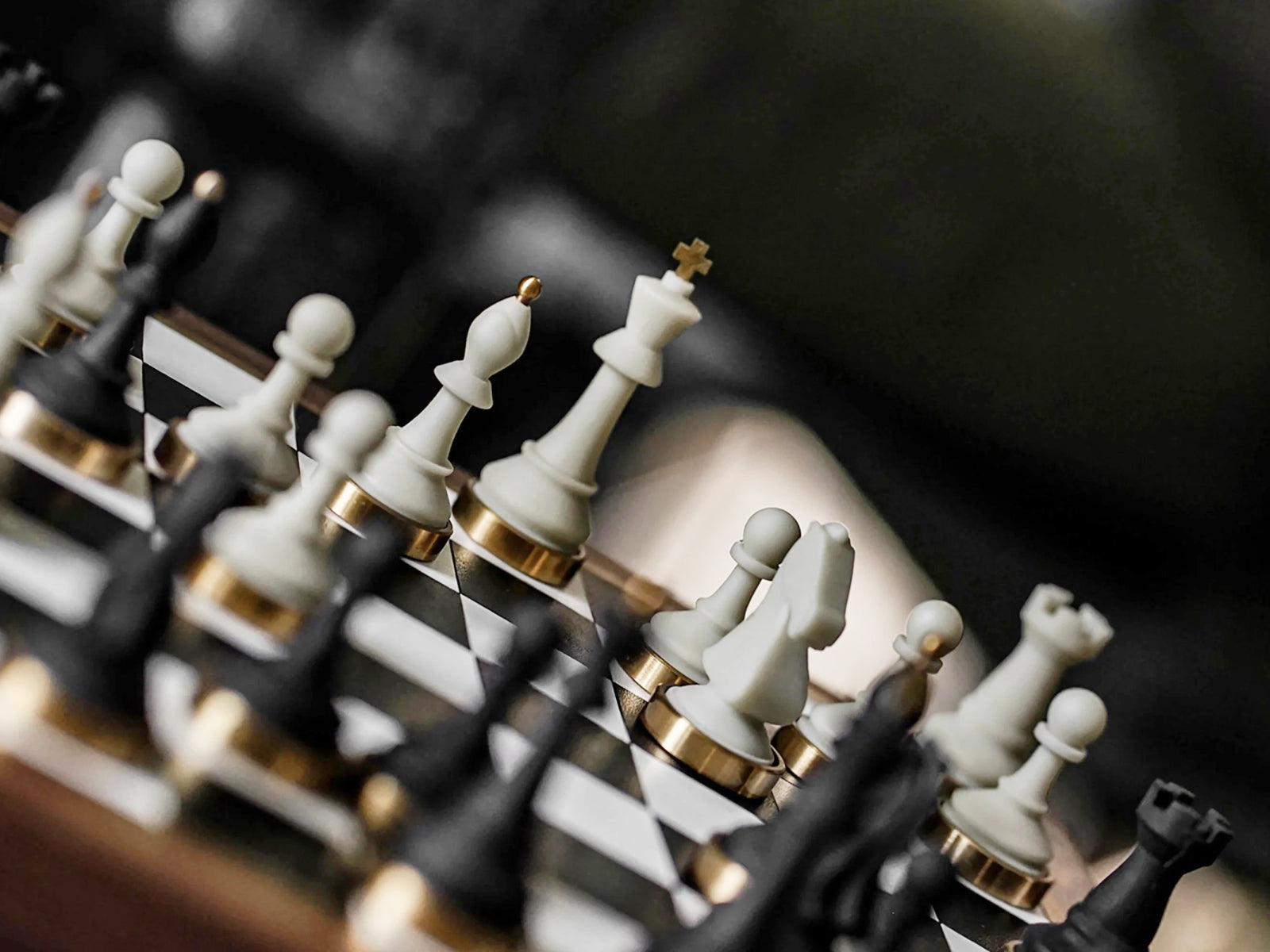 Close-up of ivory white chess pieces with gold bases along the edge of a walnut chessboard.