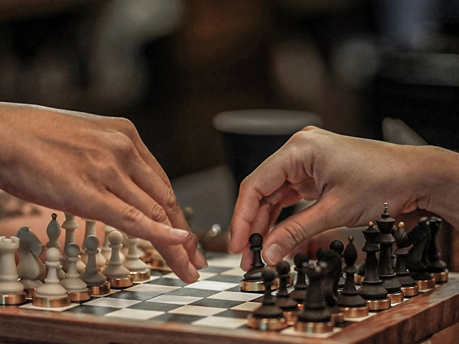 Two hands navigating a game on a premium chessboard with white and black pieces and copper bases