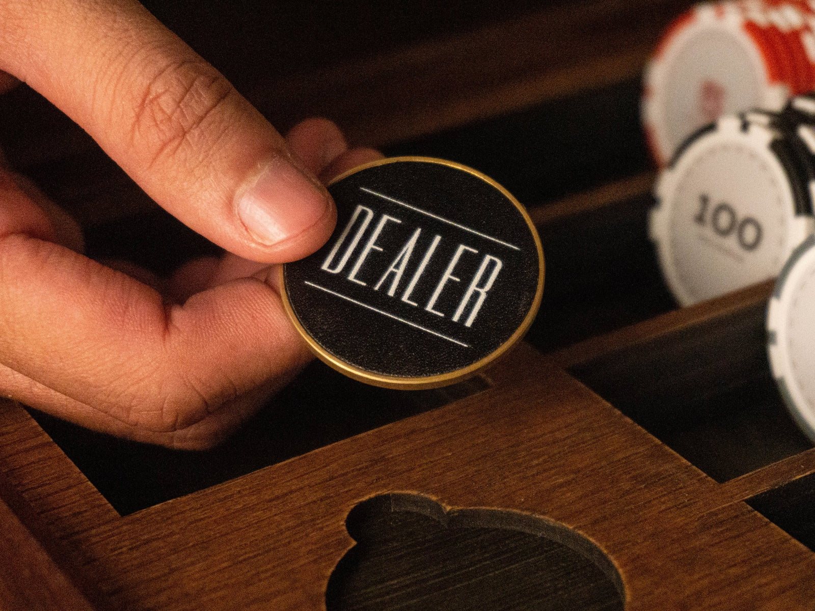 Hand places a dealer button with black face and gold rim from Bowtie Poker Chip Set on a wooden poker tray.