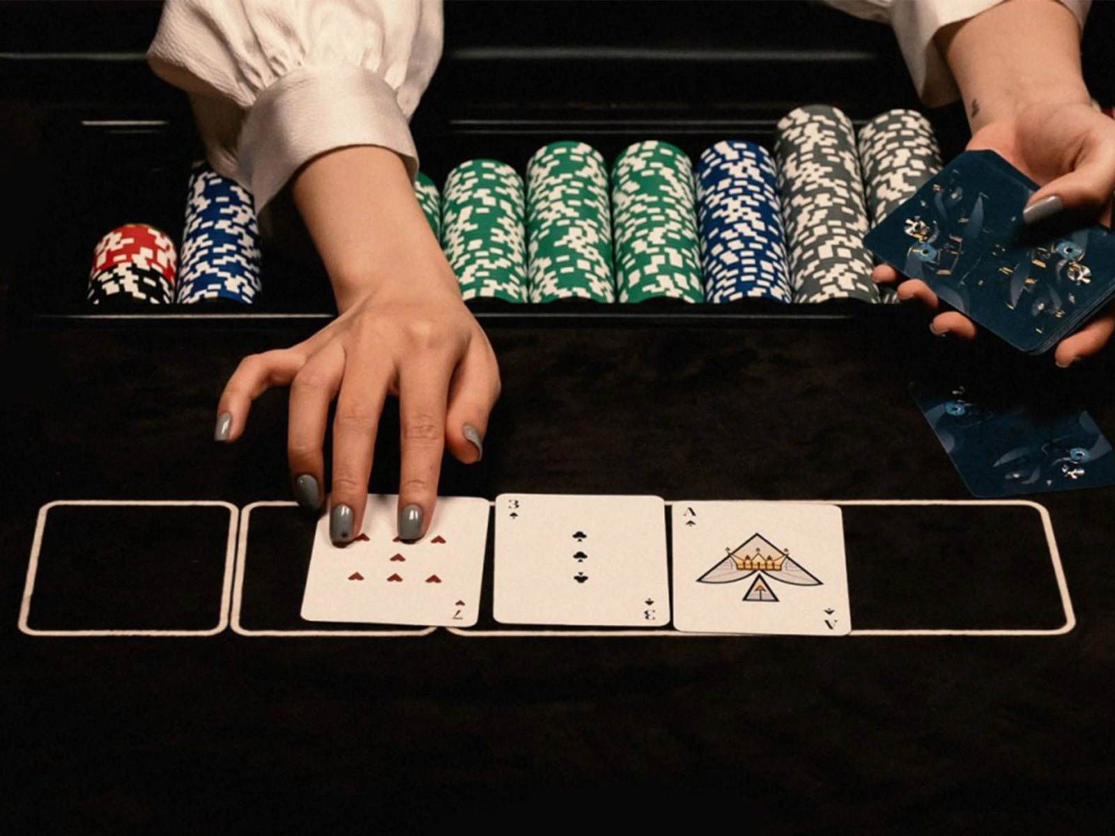 Poker table scene with a player's hand placing a card while stacks of chips line the back edge