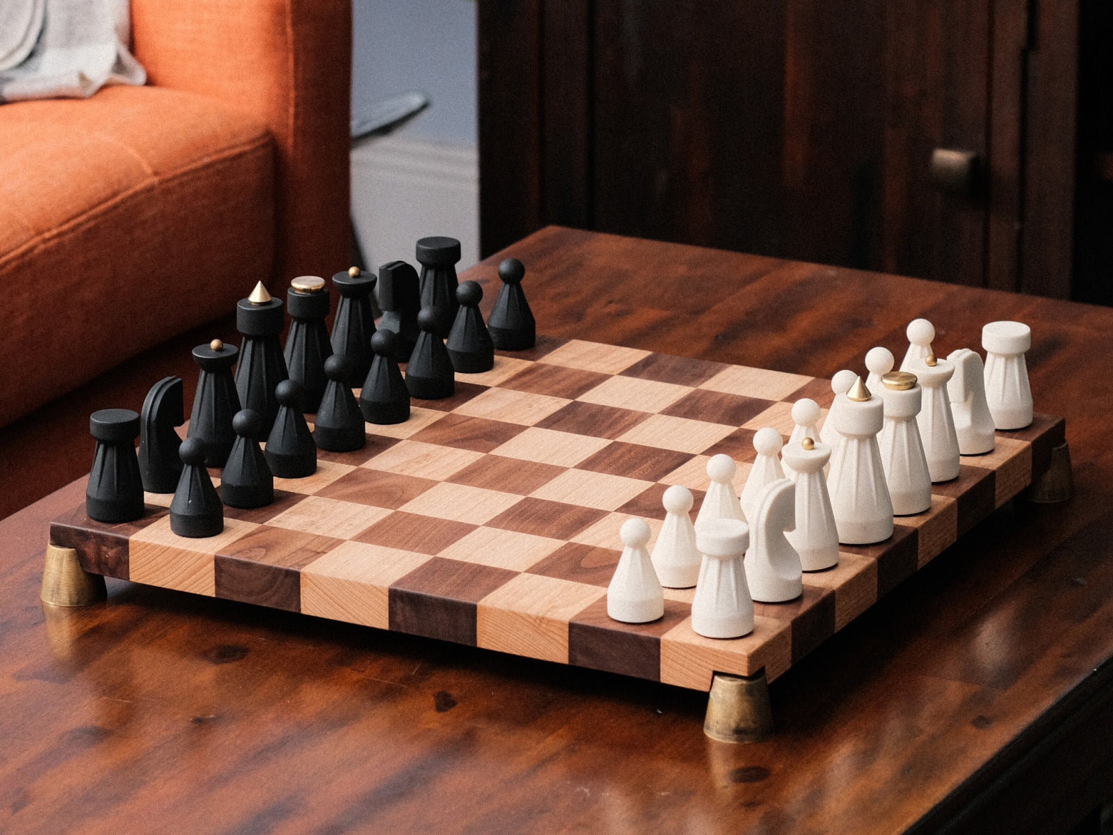 The Regal Chess Set on a two tone wooden chessboard with black and white sculpted pieces and brass feet.