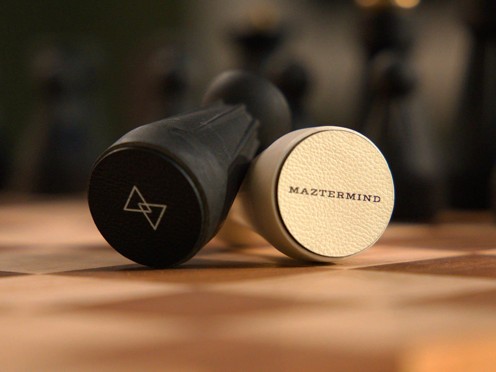 Close-up of sculptural Regal chess pieces on a wooden board, featuring a black piece and a white piece with MAZTERMIND on its base.
