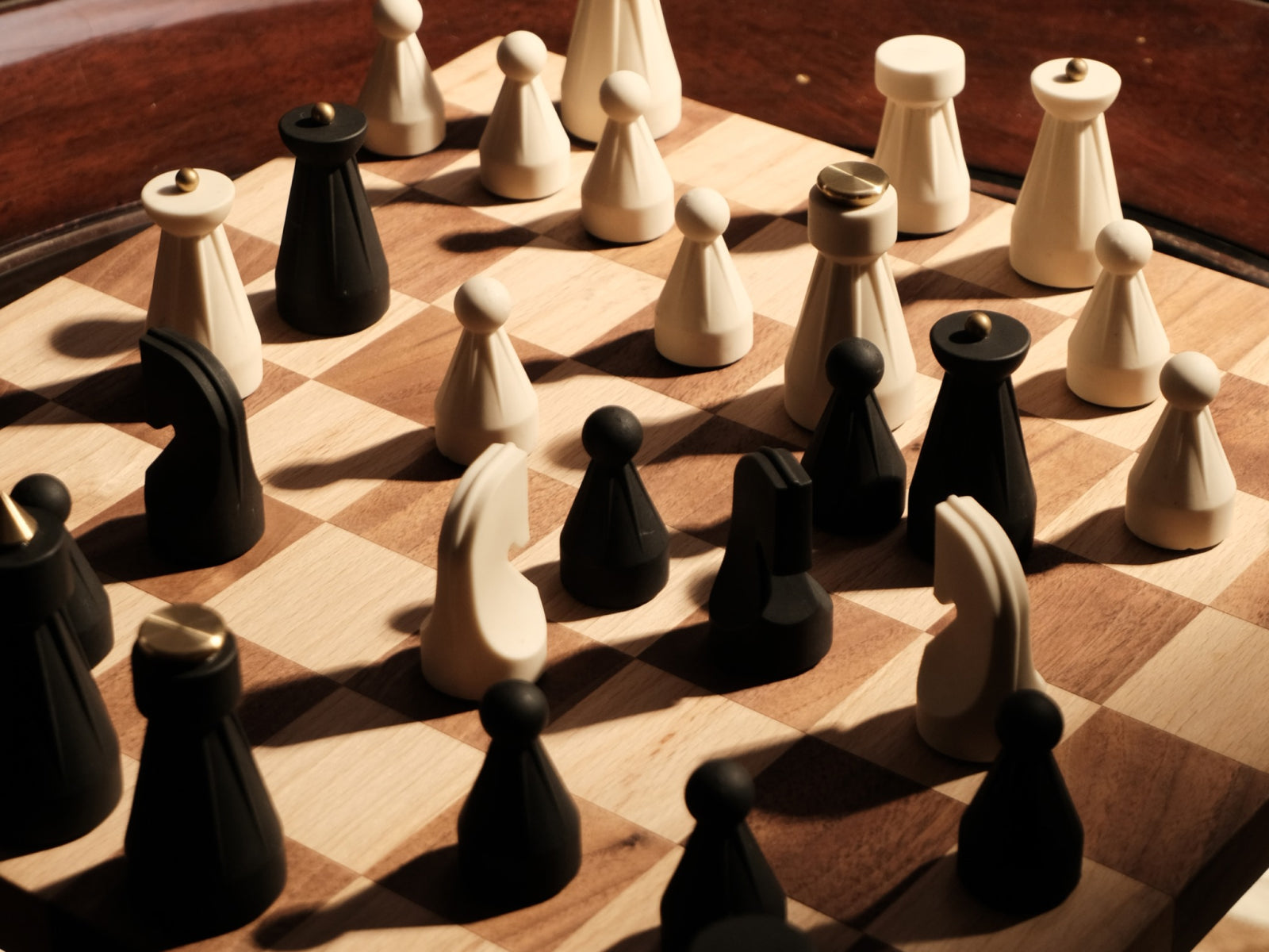 Overhead view of The Regal Chess Set on a wooden board with black and white pieces and a gold cone on a black piece