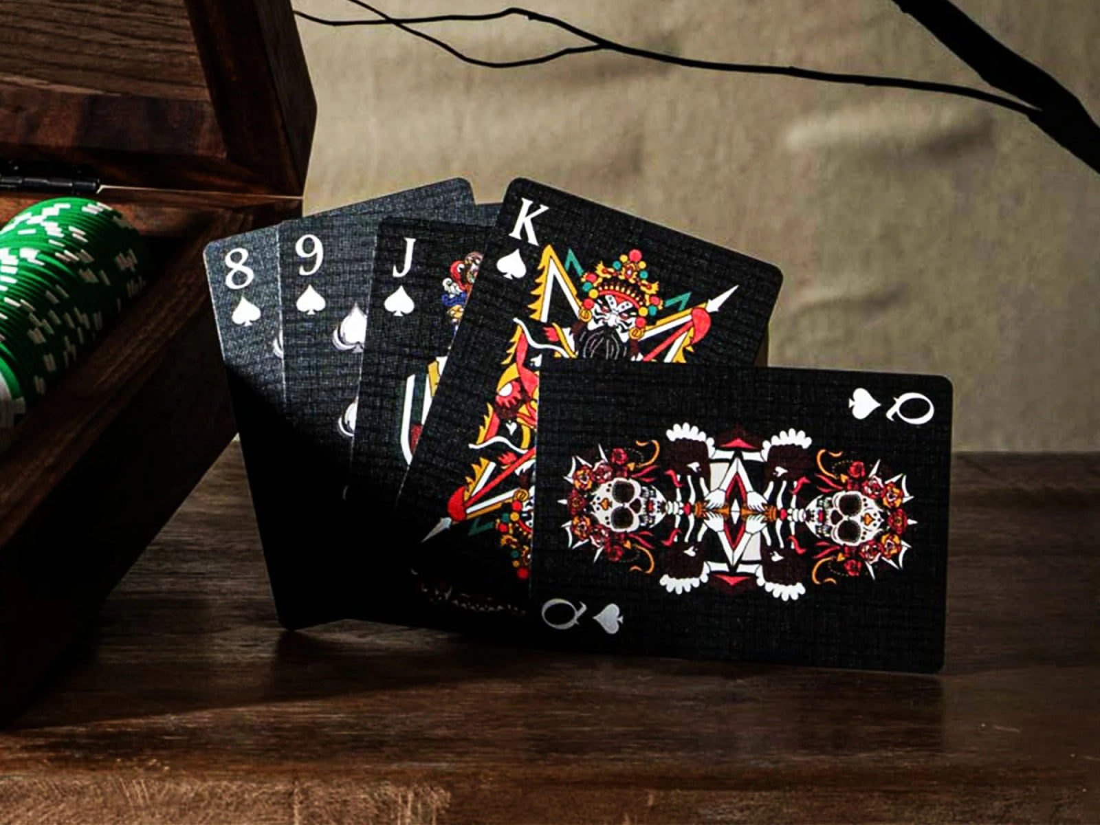 Ritual Masks playing cards spread on a wooden table with green poker chips nearby.