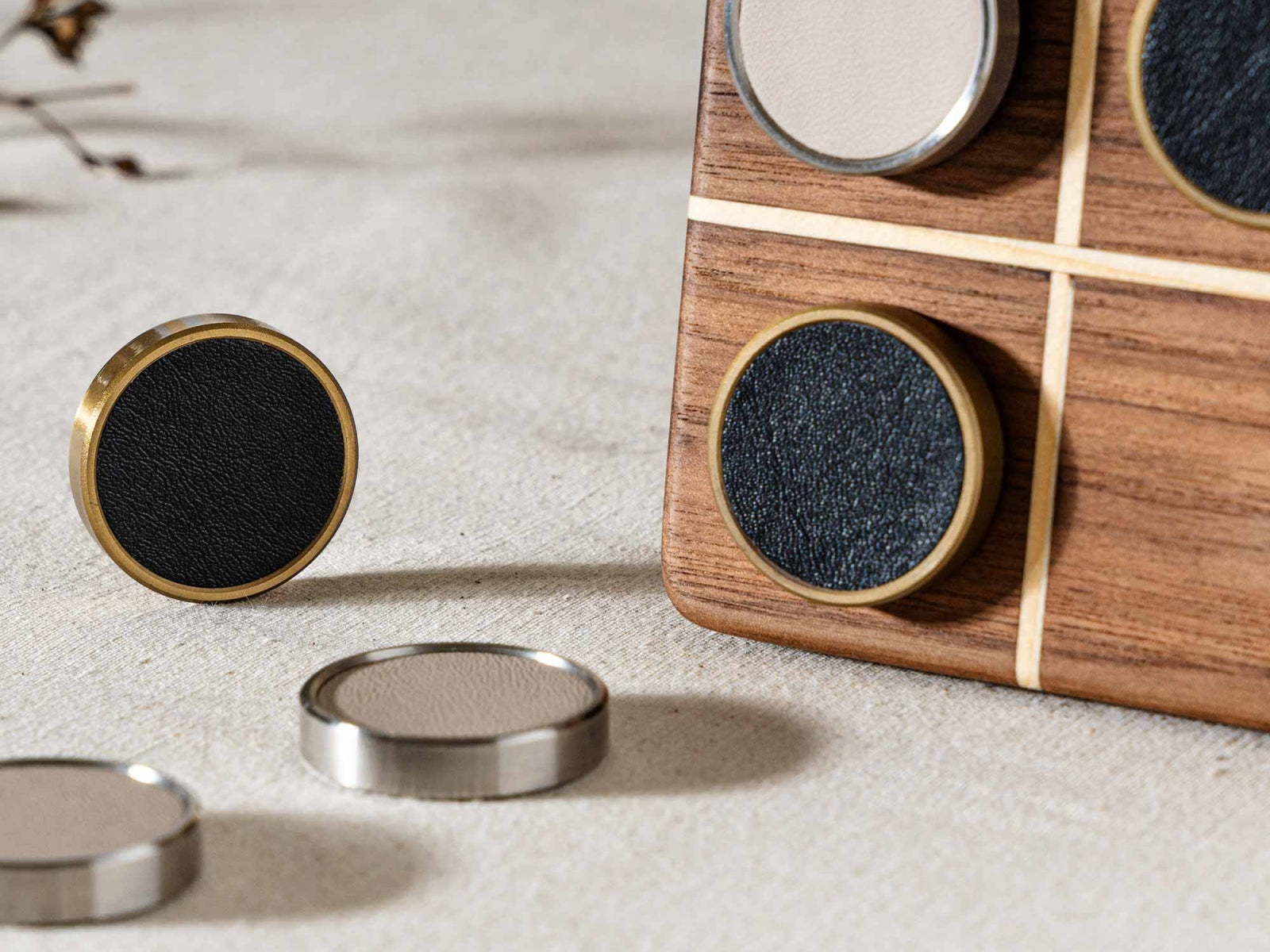 Detail of a black leather textured Tic Tac Toe token with brass edge beside a walnut pine folding board that doubles as a box