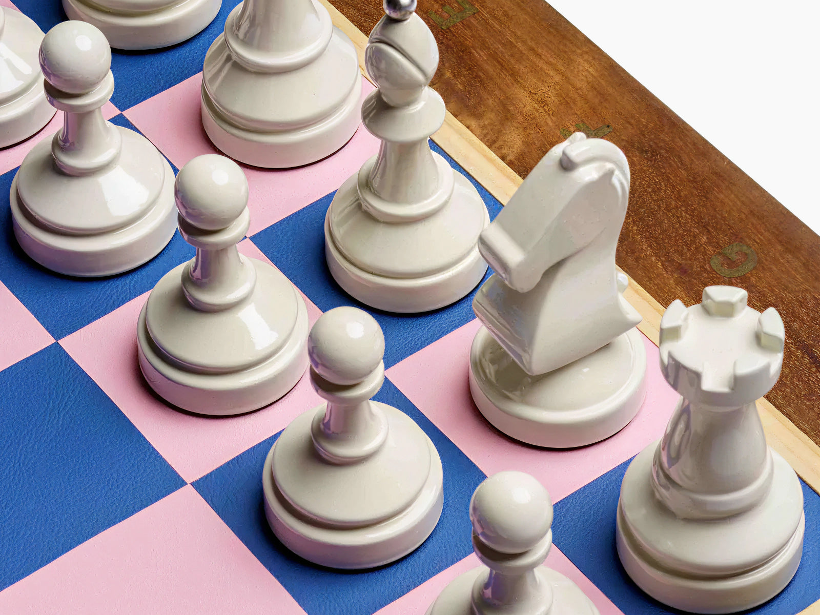 White chess pieces on a blue and pink checkered board with a wooden edge