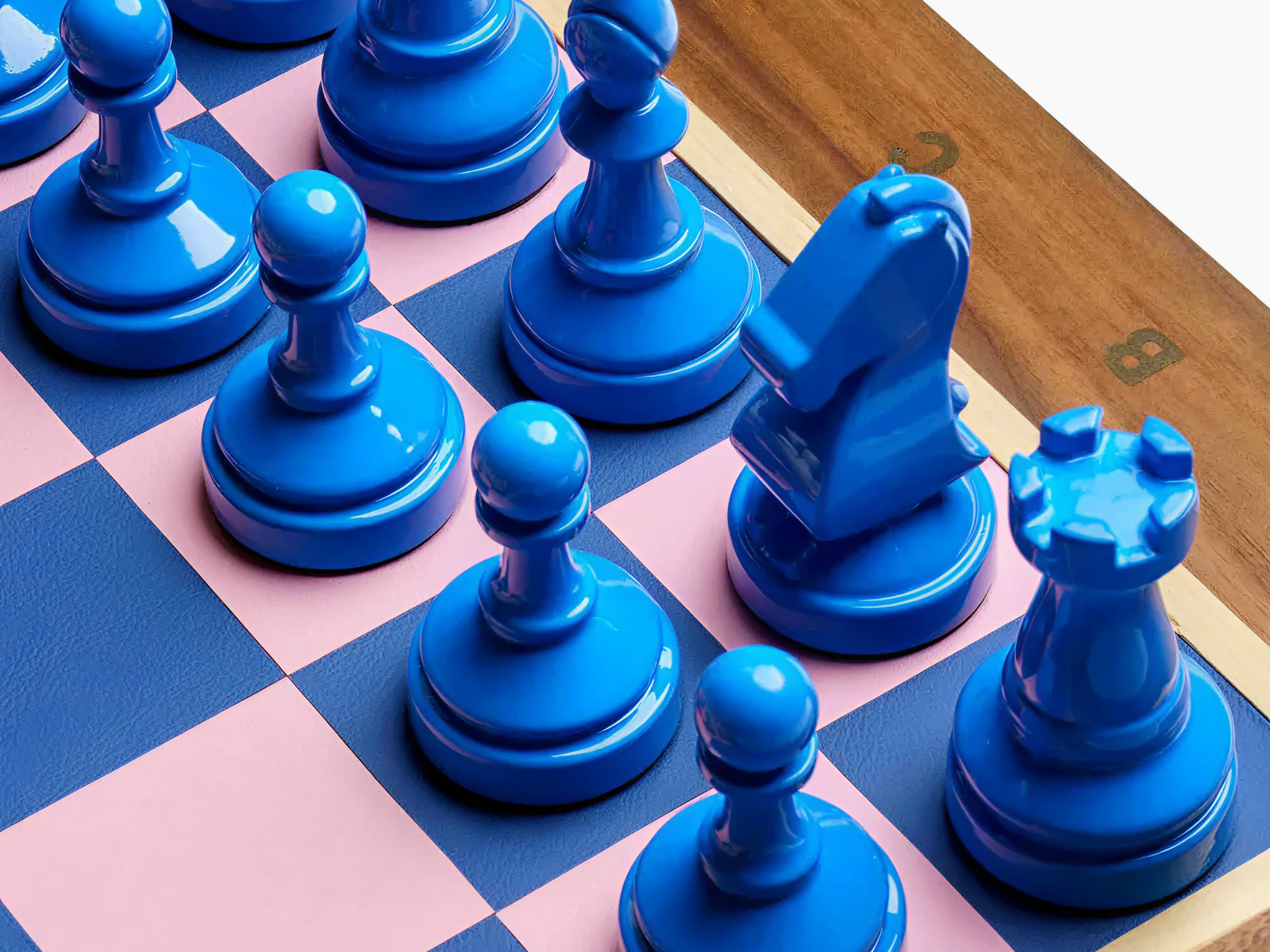 Blue glossy chess pieces on a pink and blue checkered board with a wooden edge