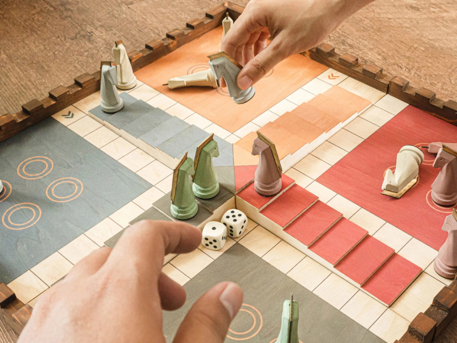Hand moves a light gray knight on a 3D pinewood Trojan Horse Race Ludo board with earth-toned cement pieces.