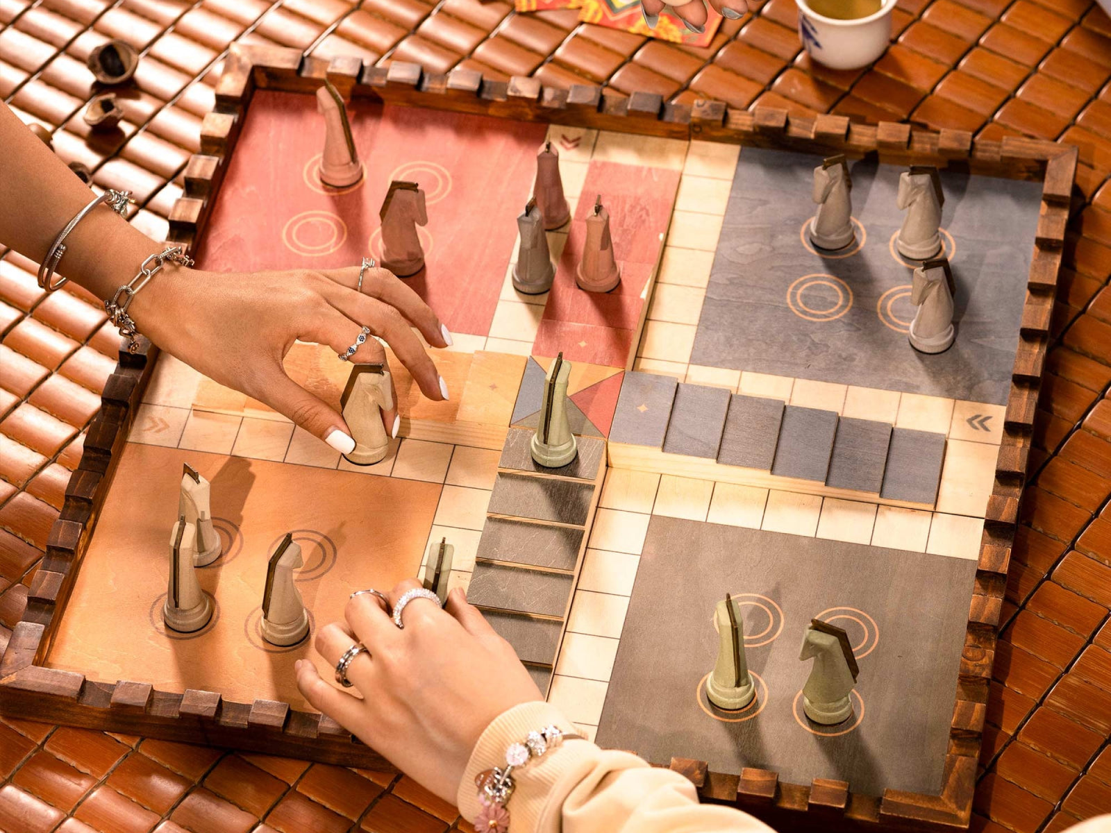 Top-down view of Trojan Horse Race Ludo board with earth-toned cement pieces and hands moving pieces across warm red and gray sections.