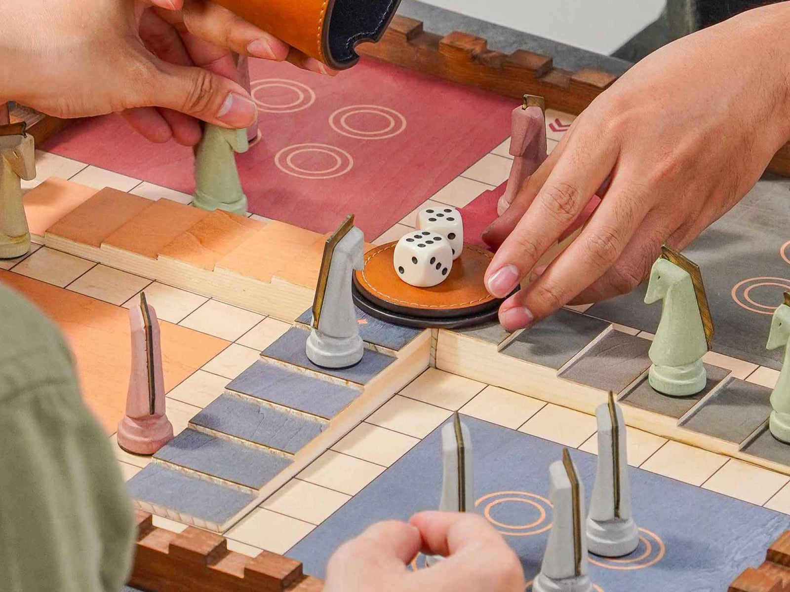 Hands move pieces on a handcrafted pinewood Trojan Horse Race Ludo board with cement pieces and a leather dice cup