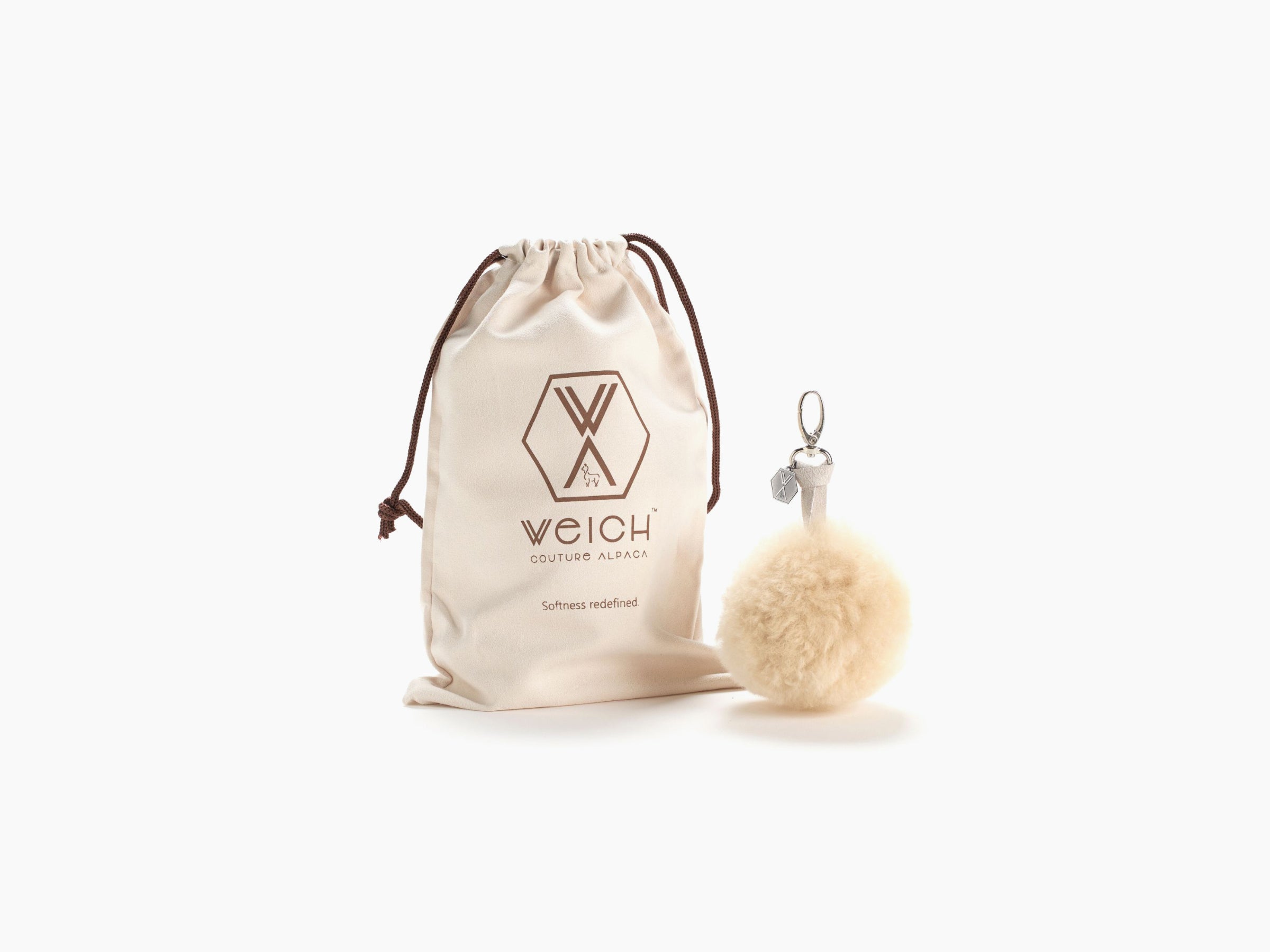 Beige drawstring pouch with brown cords beside a fluffy beige pompom CLAVE keychain.