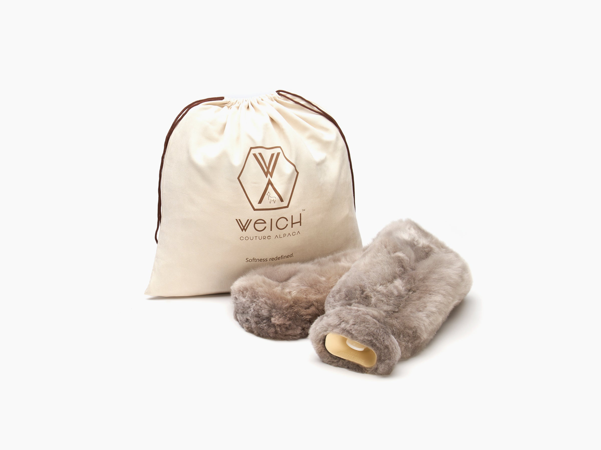 Long plush neck hot water bottle with alpaca cover beside a drawstring bag branded with Weich logo