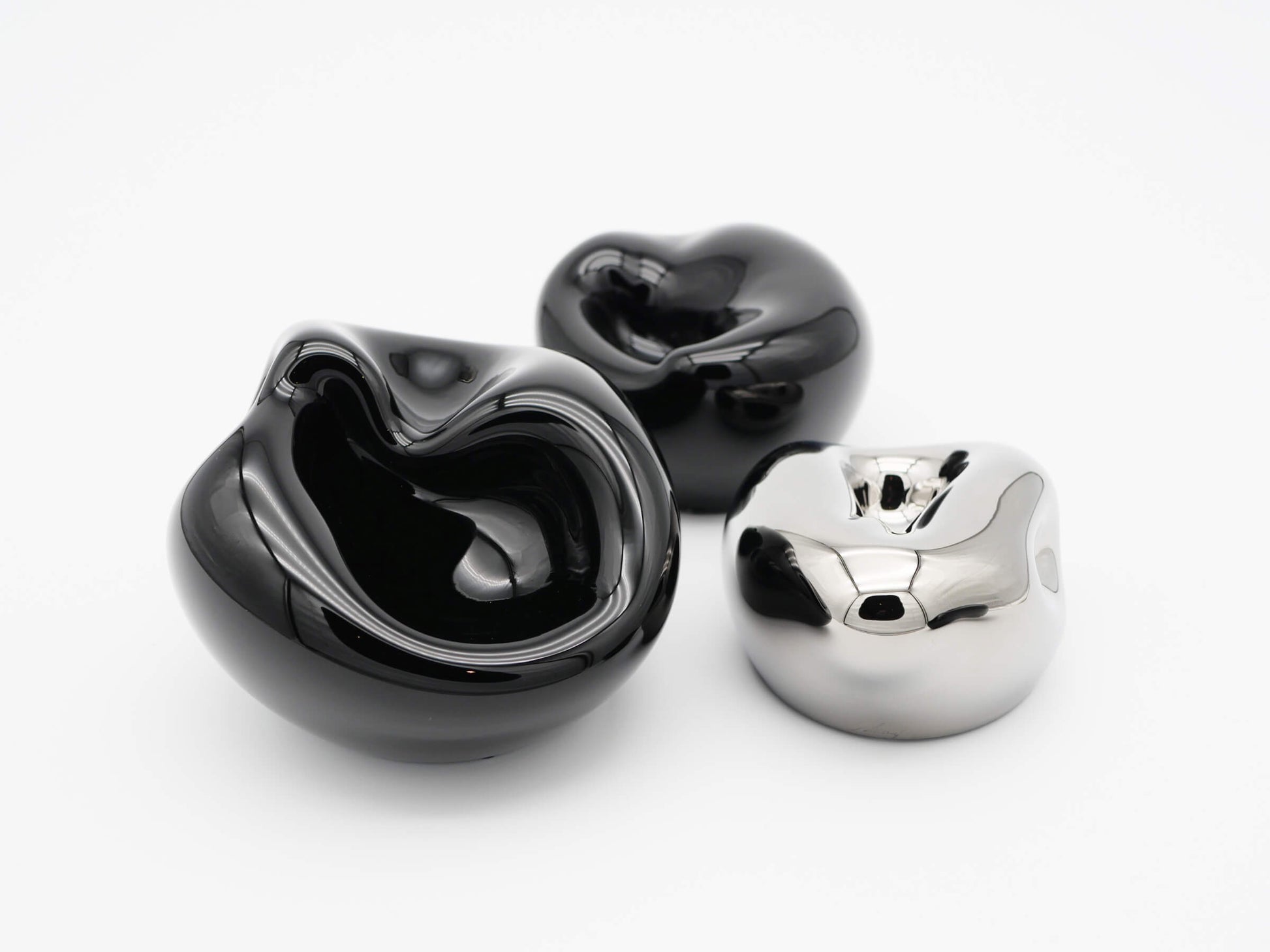 Three glossy hand blown glass vessels in obsidian black and chrome silver with flowing organic shapes.