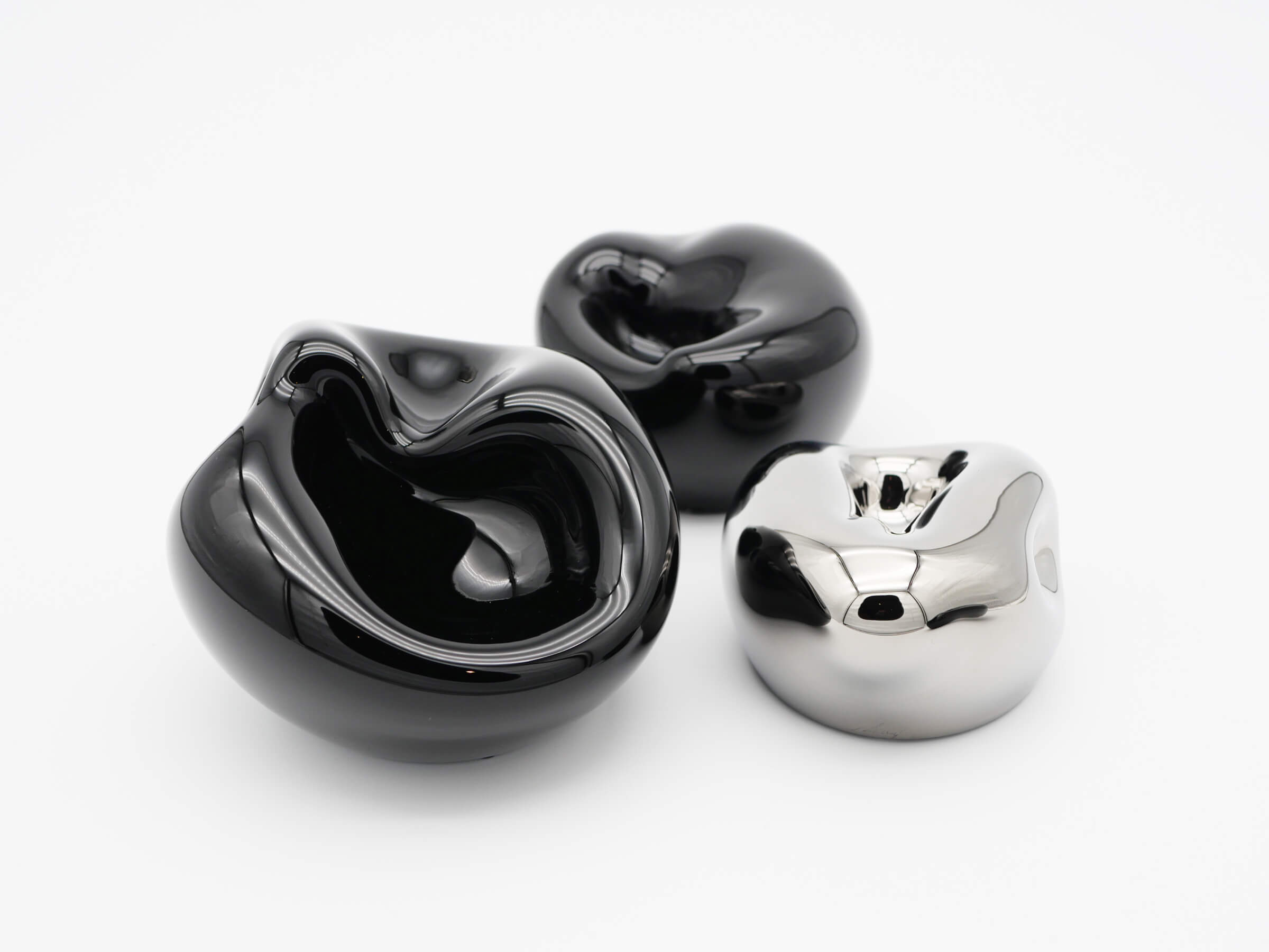 Three glossy hand blown glass vessels in obsidian black and chrome silver with flowing organic shapes.