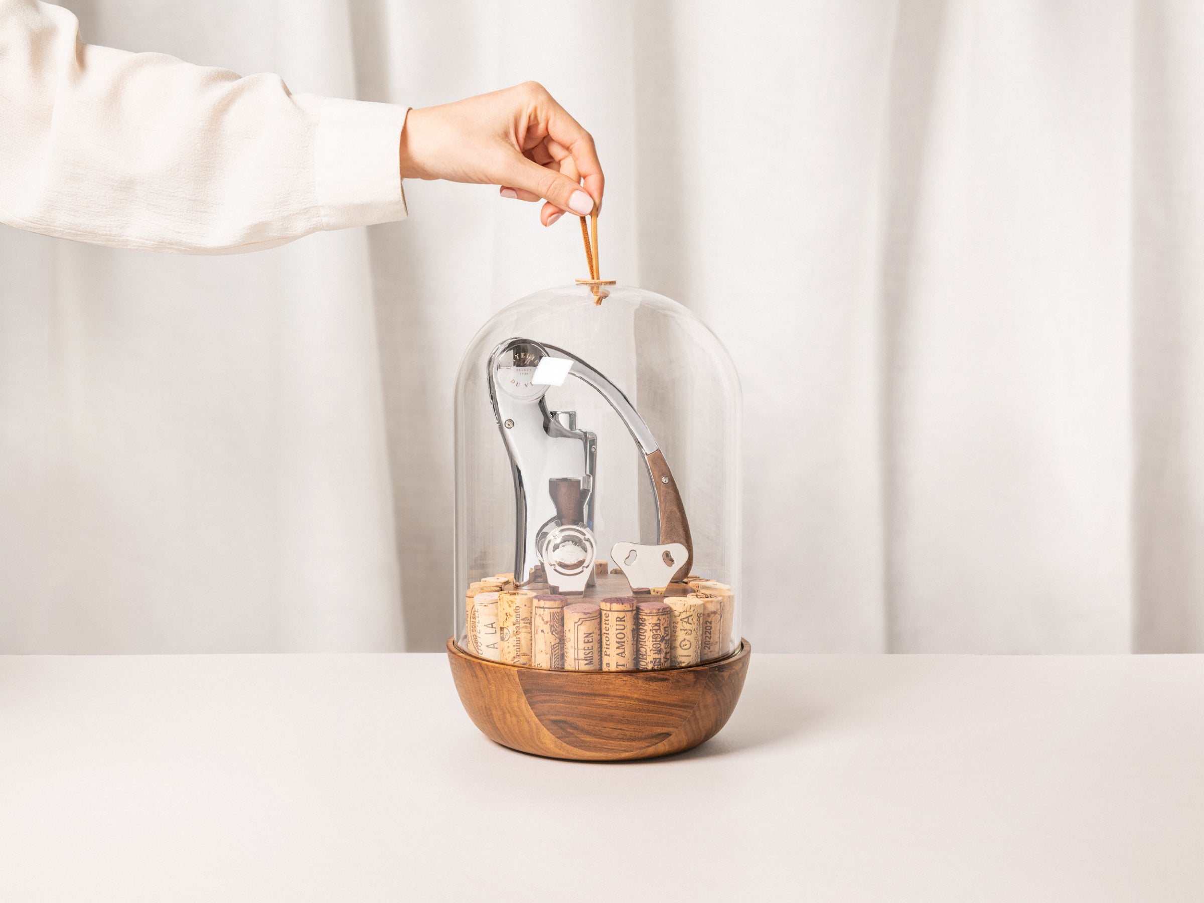 Hand lifts the glass dome of Oeno Motion Groom to reveal its wine tools.