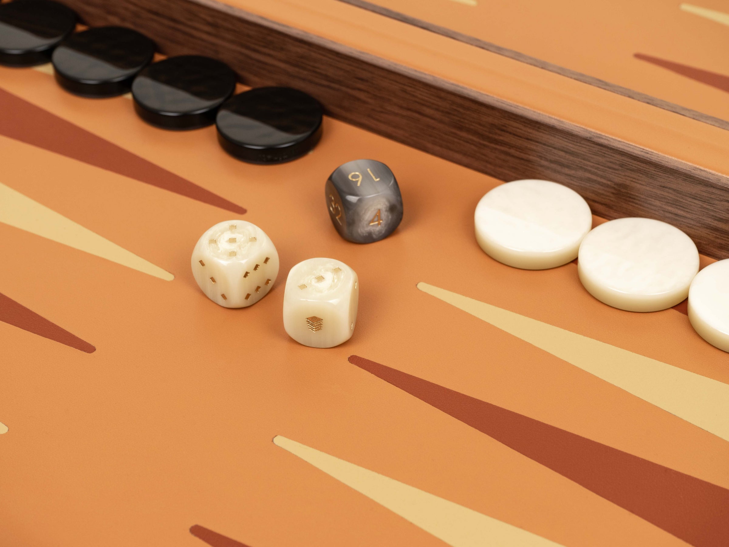 Close-up of backgammon components on an orange board with dark checkers and ivory pearled pawns beside a gray marbled die and two white dice.