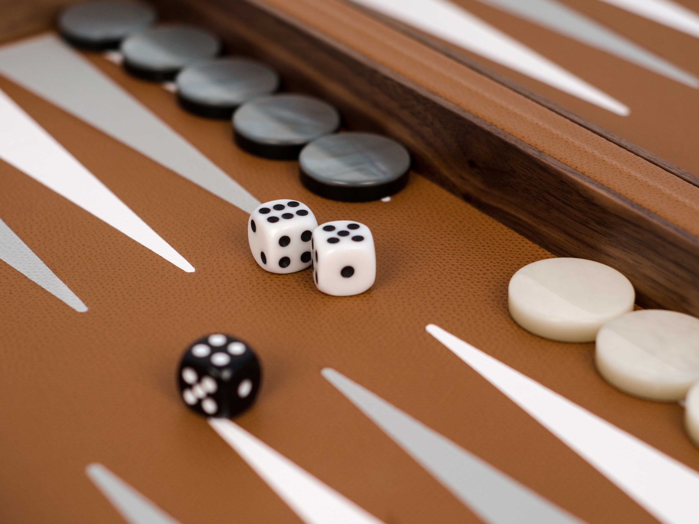 White dice with black pips and pearl pawns on a brown walnut backgammon board.