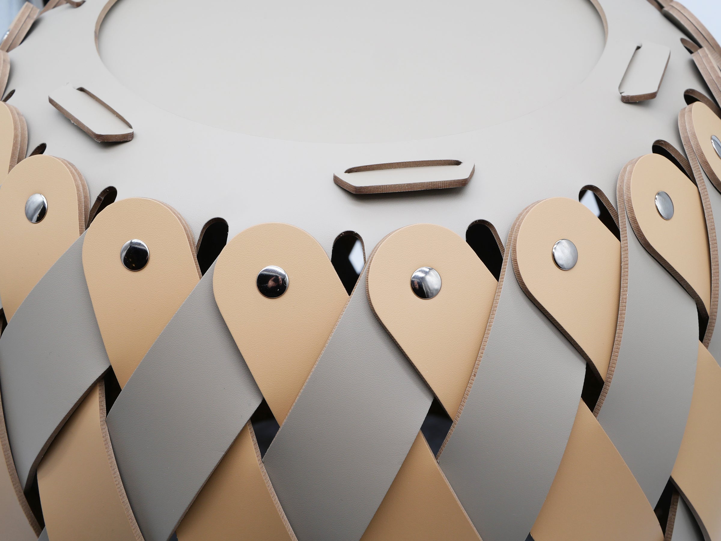 Close up of the Canaria Medium Basket showing interwoven tan and gray leather strips with metal rivets.
