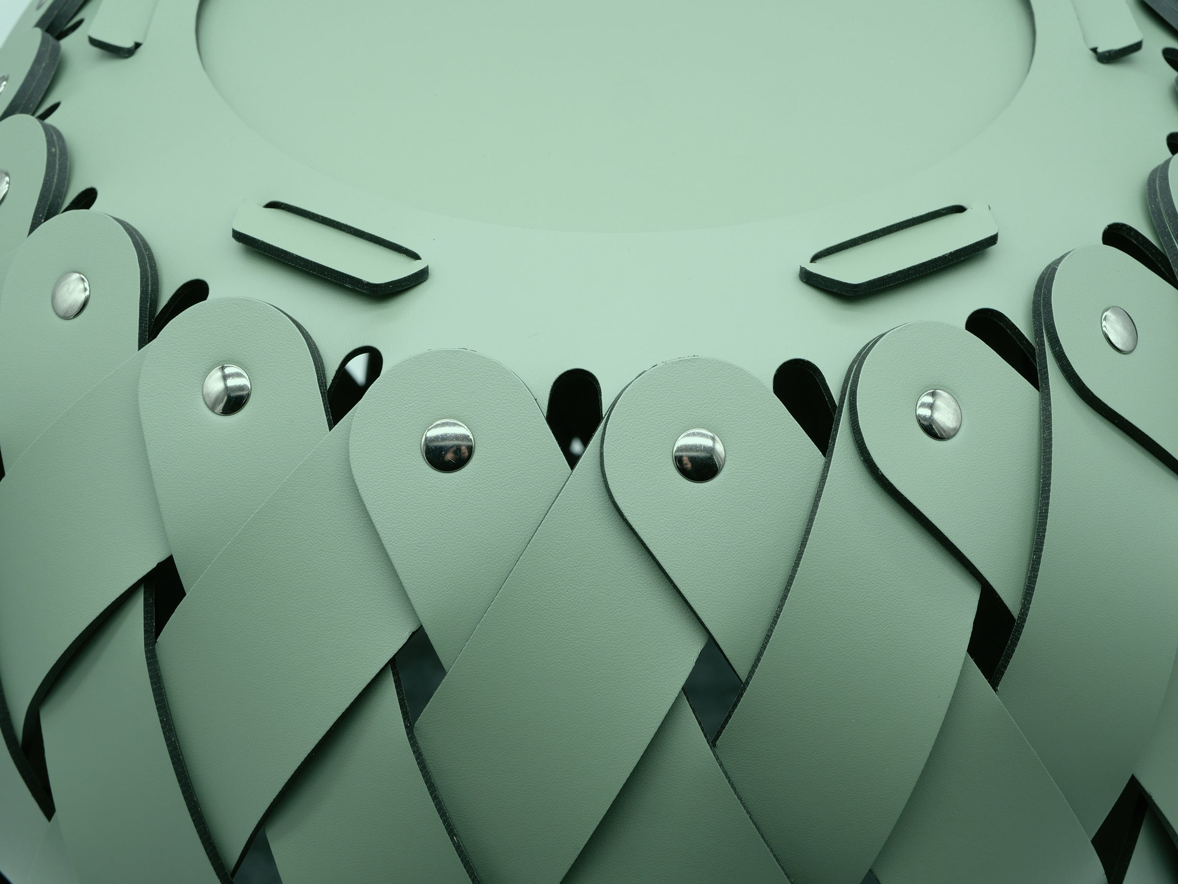 Close-up of green braided Antibes leather strips with metal rivets forming the Canaria basket texture