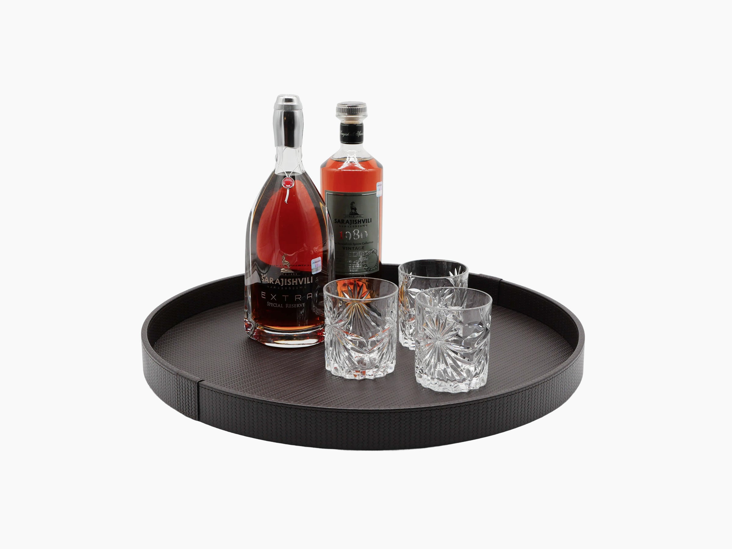 Round leather upholstered tray on a wooden base with two liquor bottles and four crystal tumblers.