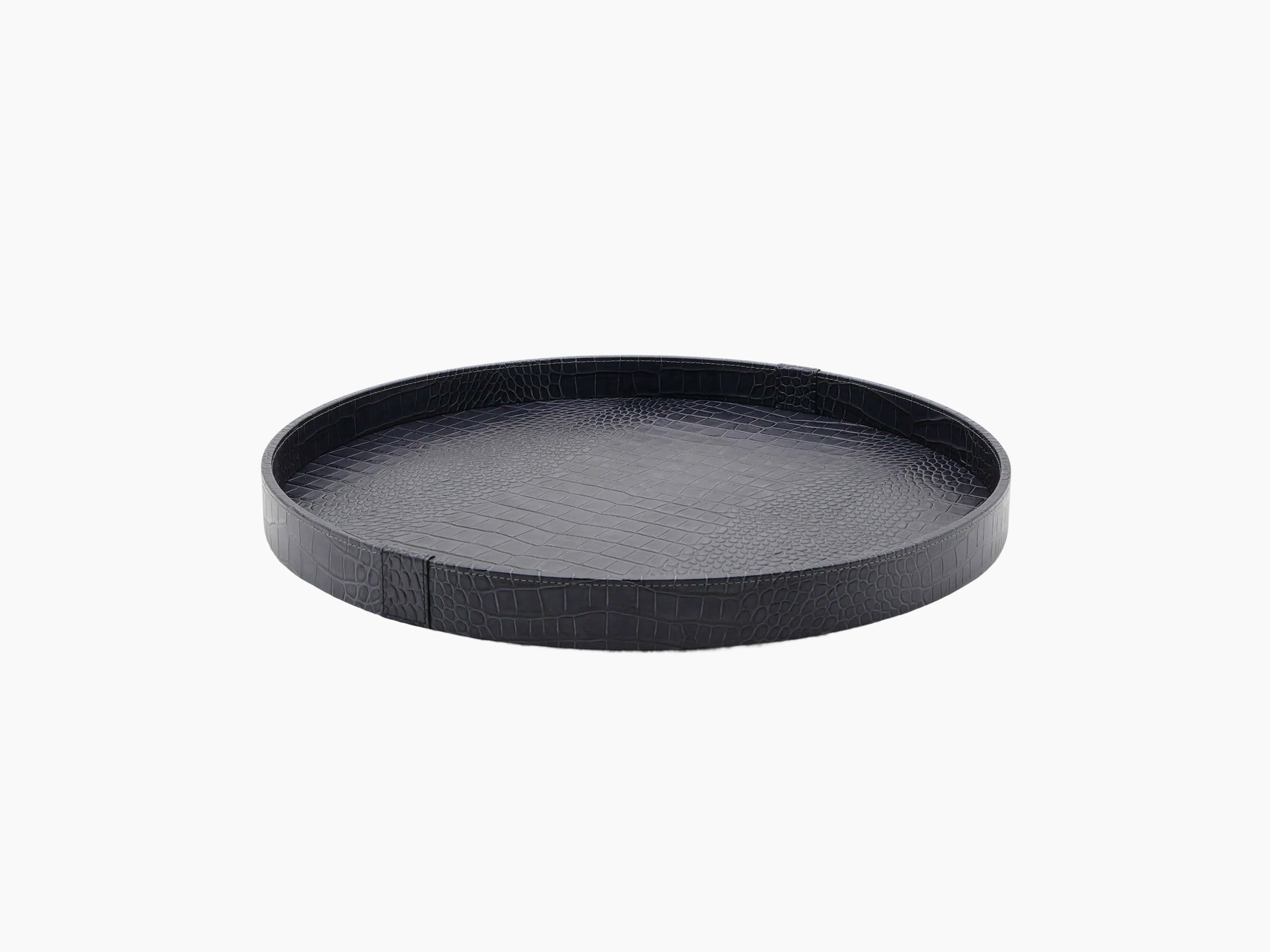 Dark round leather tray with crocodile texture on a wooden base.