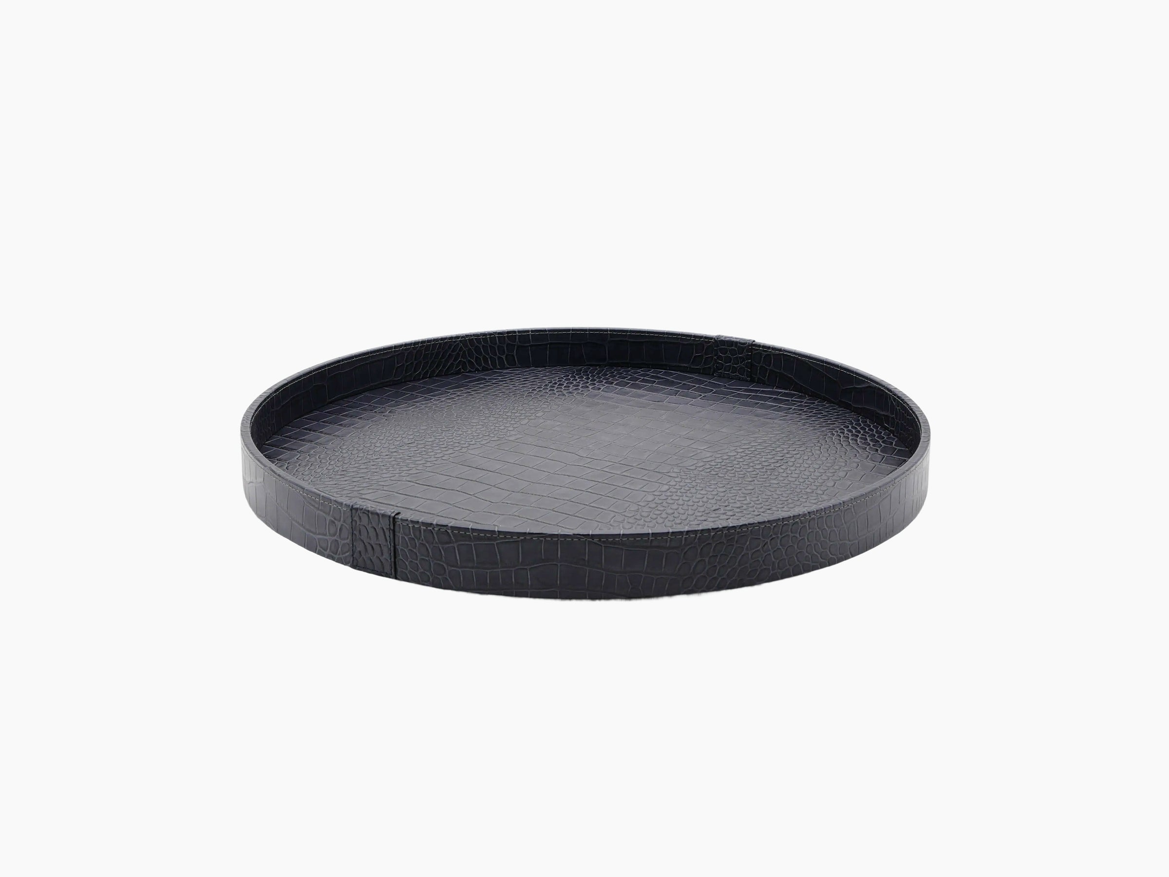 Dark round leather tray with crocodile texture on a wooden base.