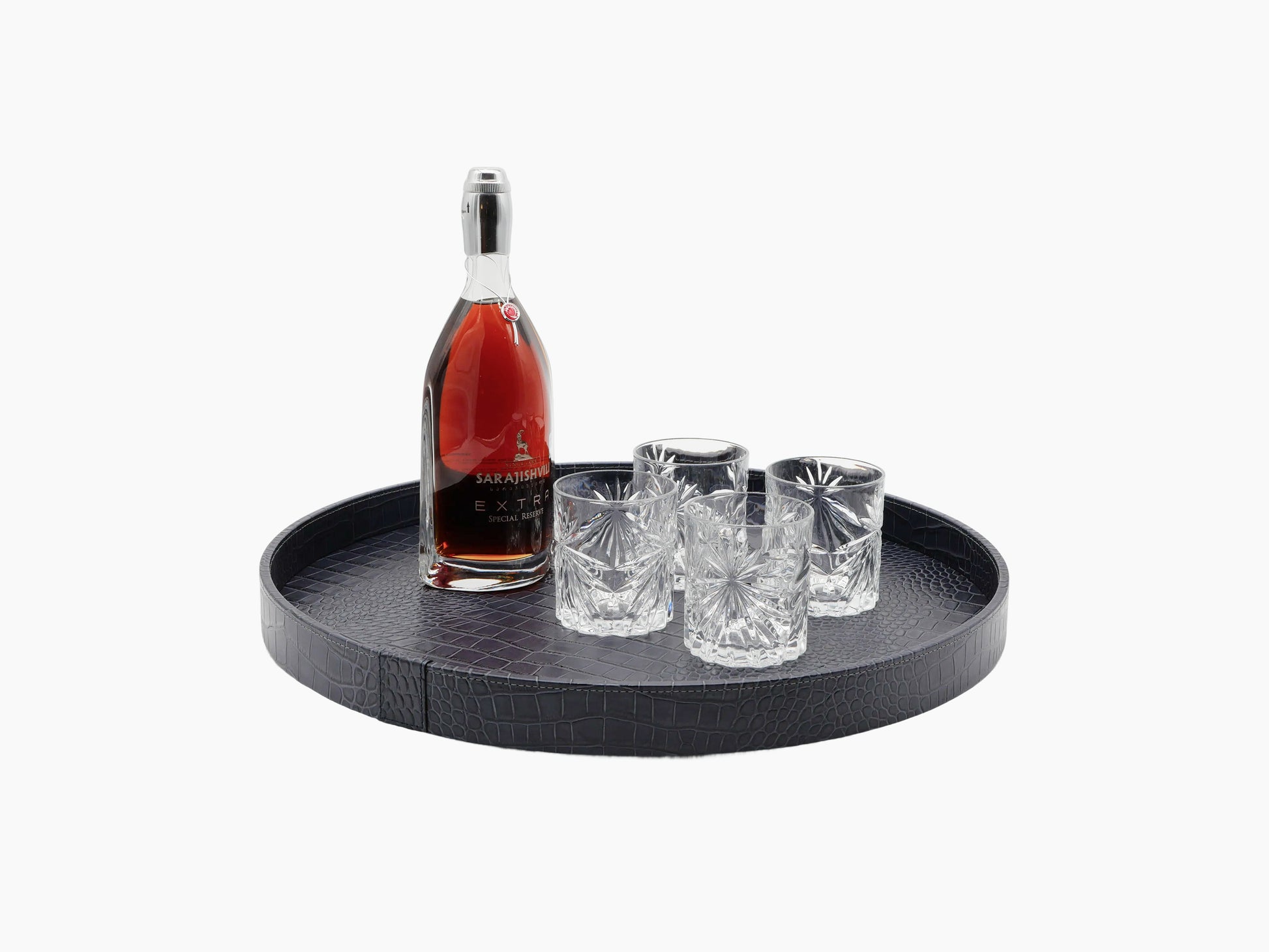 Large dark leather round tray with crocodile texture holding a whiskey bottle and four crystal glasses