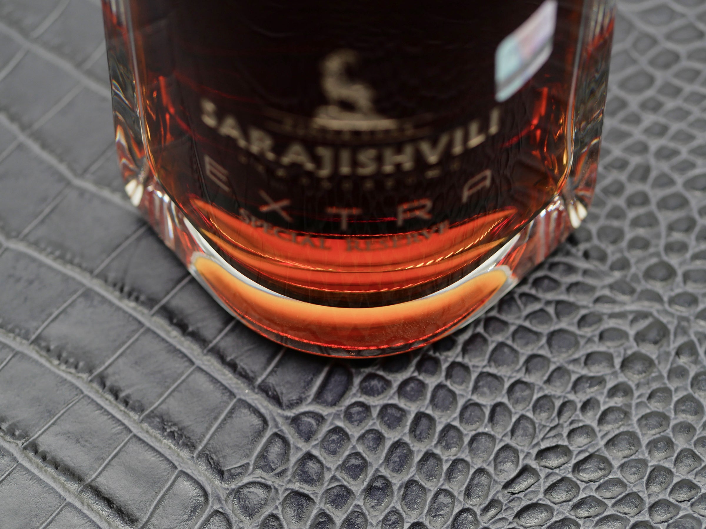 Close up of a glass bottle with amber liquid on a dark crocodile textured surface.