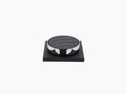 Round leather coaster resting on a chrome framed holder on a dark wooden base