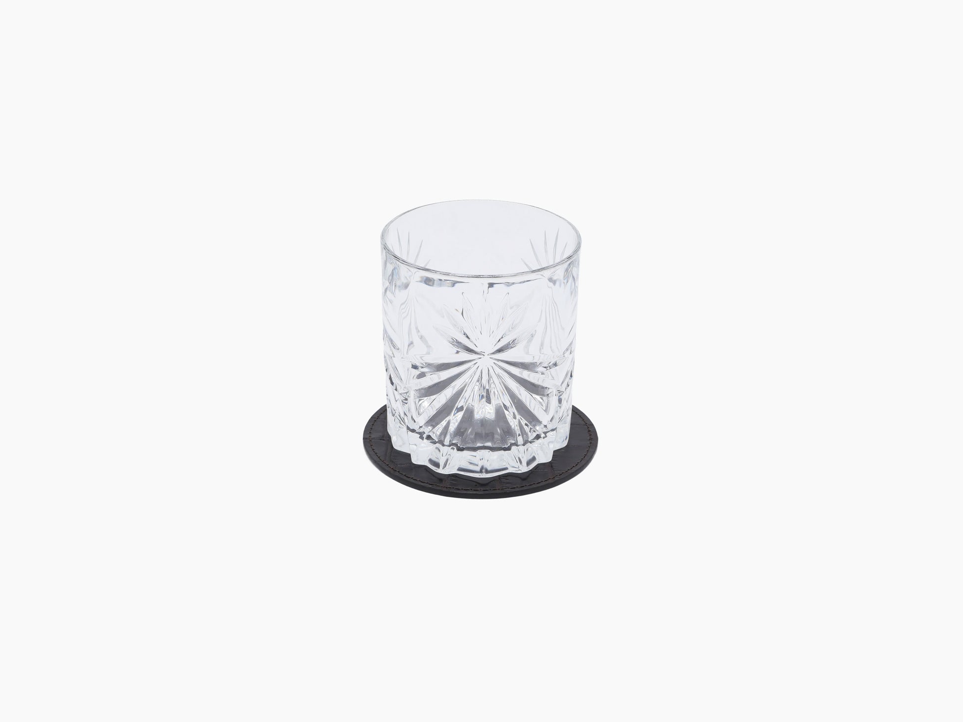 Crystal tumbler on a round dark leather coaster.