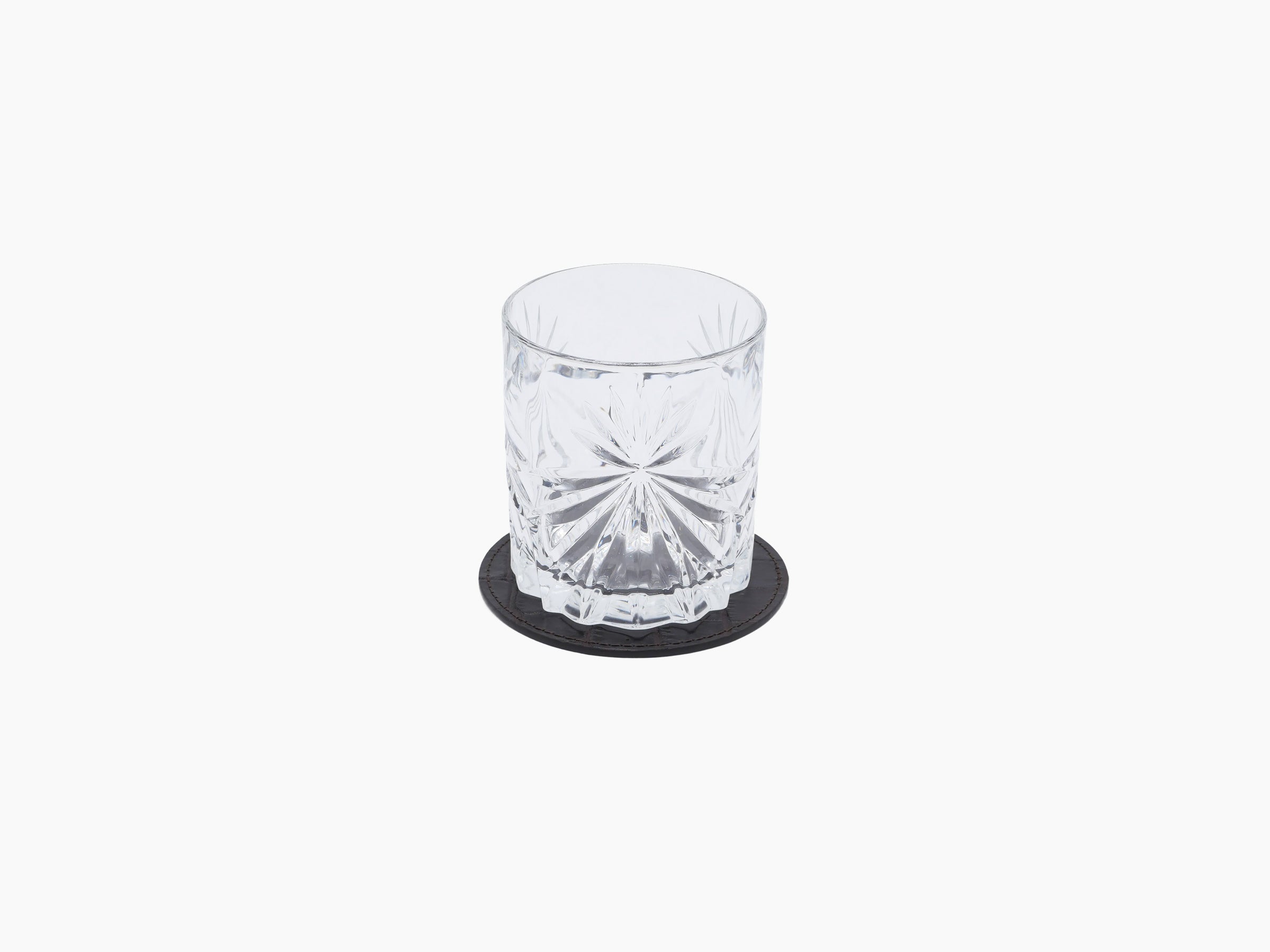 Crystal tumbler on a round dark leather coaster.