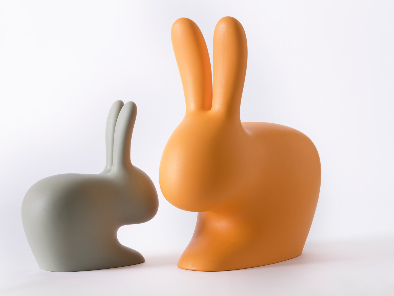 Orange Baby Rabbit Chair beside a smaller pale green Rabbit Chair on a white backdrop.